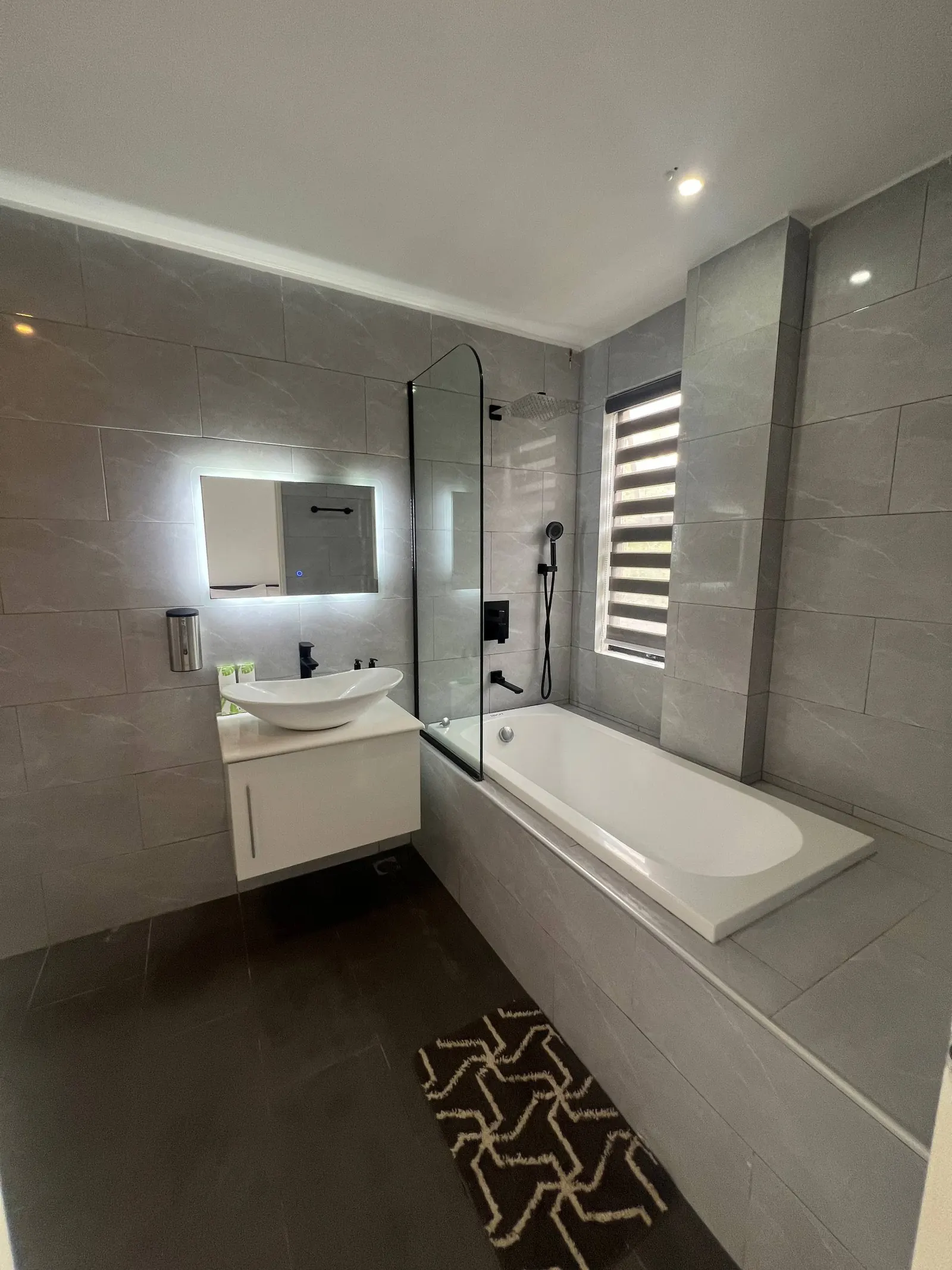 En-suite vanity, mirror and bathtub with glass screen